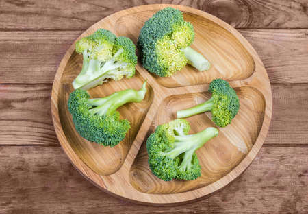 Small branches with inflorescences of the fresh raw broccoli on the wooden compartment dish on...