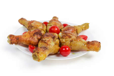 Grilled crispy chicken legs laid out with cherry tomatoes on the white dish on a white background, close-up in selective focusの写真素材