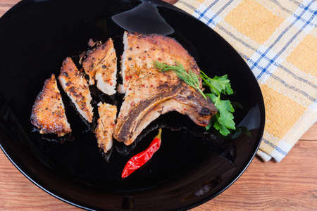 Grilled pork loin chop bone-in, partly cut on the black dish close-up