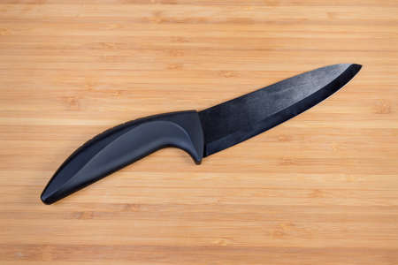 Modern kitchen knife with black colored ceramic blade and plastic handle on the bamboo wooden...