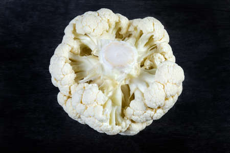 Whole head of the fresh raw cauliflower with a cabbage stalk up, close-up on a black surfaceの写真素材