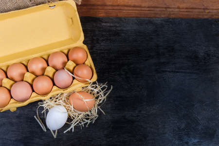 Chicken eggs in open egg carton, eggs on wood shavings beside to her on the dark surface, located left with empty the rest of, top view, backgroundの写真素材