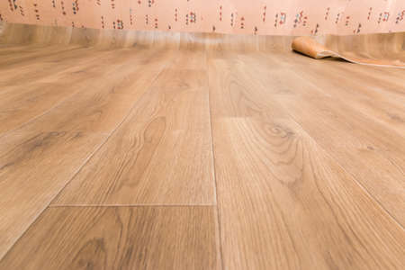 Sheet vinyl flooring with embossed imitation of wooden planks pattern during laying, fragment, low point view in selective focus
の写真素材