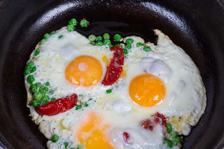 Fried eggs prepared by sunny side up with green pea and sun-dried tomatoes in the rustic cast frying...