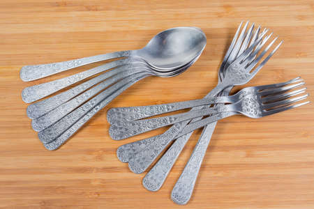 Stainless steel eating utensils consisting of spoons and forks on the wooden surface, top view