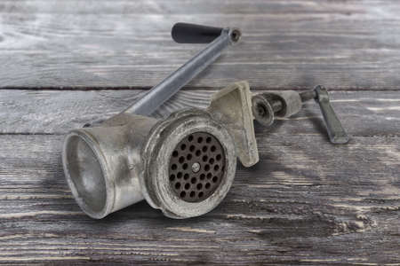 Vintage hand-powered meat grinder assembled for use lying on the old rustic table, close-up at selective focusの写真素材