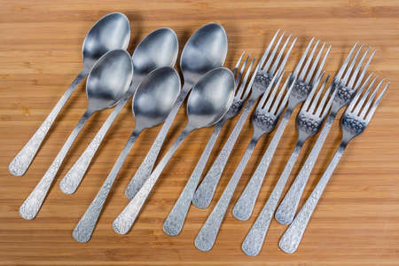 Stainless steel eating utensils consisting of spoons and forks laid out on the wooden surface, top...