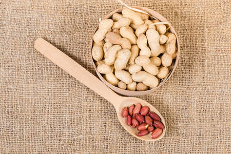 Dried peanuts in their shells in small round wooden box and peeled nuts in the wooden spoon on the...