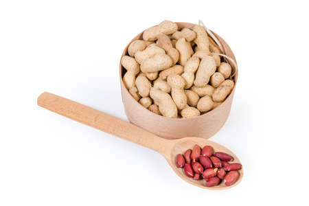 Dried peanuts in their shells in small round wooden box and peeled nuts in the wooden spoon on a...