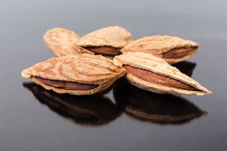 Several whole dried mountain almonds in their shells close-up in selective focus on a dark...