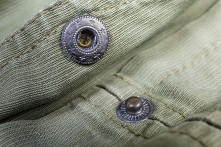Two collapsible parts of the unbuttoned metal snap button fastener, mounted on the outerwear olive color close-up at shallow depth of field
の写真素材