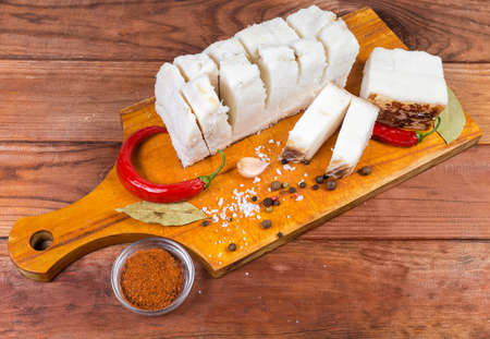 Pieces of partly cut salted pork fatback on skin lie on wooden cutting board among the some spice on the rustic tableの写真素材