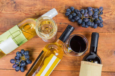 Corked bottles of the red and white wine lie on their side, wine glasses of wine are standing among...
