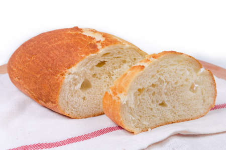 Half and slice of oval loaf of wheat bread on the cloth napkin on a white background