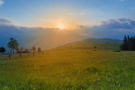 Highland glade with fences and rural buildings at summer sunrise in the Carpathian Mountains