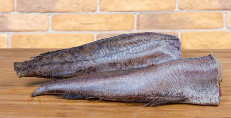 Two defreezed uncooked carcasses of the hake without of the heads and tails on the wooden surface...