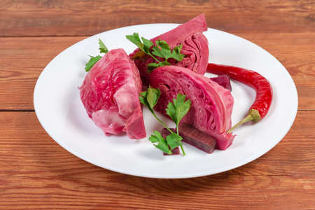 Pieces of heads of white cabbage pickled with beetroot on the dish close-up on the old rustic tableの写真素材