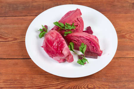 Pieces of heads of white cabbage pickled with beetroot on the dish close-up on the old rustic tableの写真素材