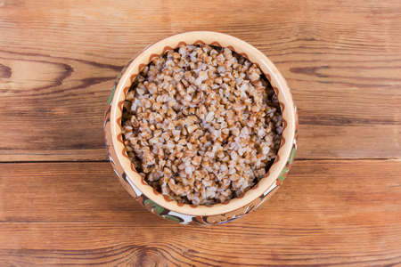 Buckwheat porridge in the clay glazed bowl decorated with a pattern on the rustic table, top viewの写真素材