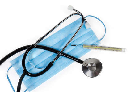 Stethoscope and classic mercury clinical thermometer lie on the disposable medical mask, top view