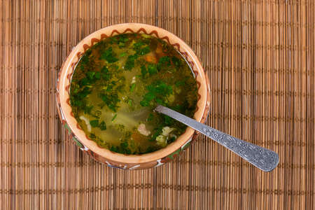 Homemade chicken soup with noodle in the brown clay bowl with spoon on the bamboo table mat, top viewの写真素材