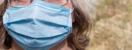 Light blue disposable medical mask wearing on a face located left on a blurred background of trees, close-up in selective focusの写真素材