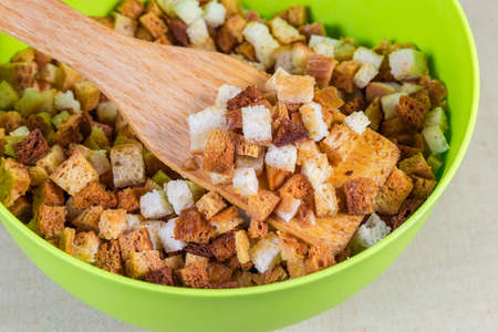 Homemade pieces of dried bread crumbs in the form of small cubes with wooden kitchen spatula in the plastic bowl, close-up in selective focus
の写真素材