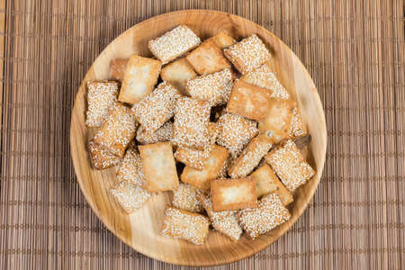 Flat rectangular flaky crispy cookies with candied roasted sesame on the wooden dish on the bamboo table mat, top viewの写真素材