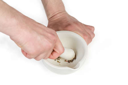 Pestle and porcelain kitchen mortar in hands during spices grinding on a white backgroubd, close-up in selective focus
の写真素材