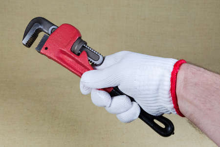 Modern heavy duty pipe wrench with steel hardened serrated jaws in hand wearing a knitted protective household gloveの写真素材