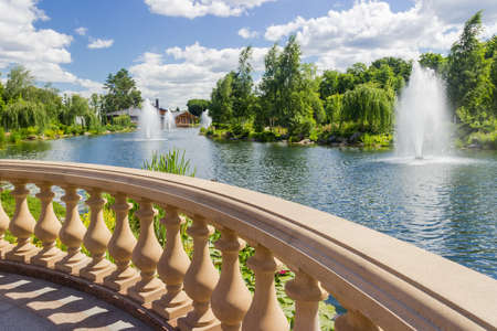 Fragment of stone balustrade with shaped balusters over the decorative pond with fountains in summer park
の写真素材