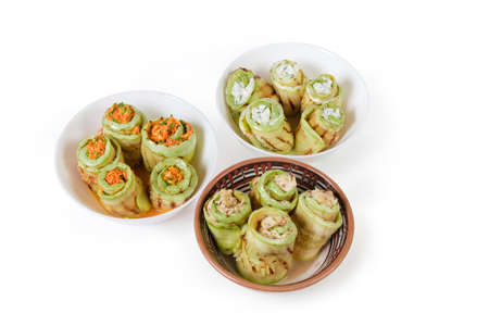 Rolls of grilled long slices of vegetable marrow with various filling lie in the three different bowls on a white backgroundの写真素材