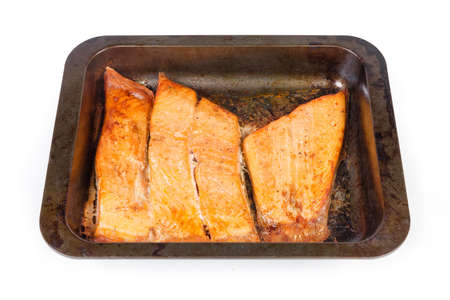 Baked pieces of the trout fillet on the rustic metal oven tray on a white background