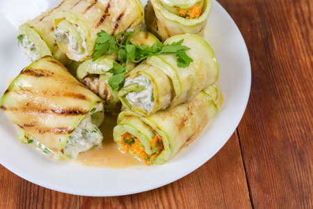 Rolls of grilled long slices of zucchini with various filling lie on dish on the rustic table, fragment close-upの写真素材