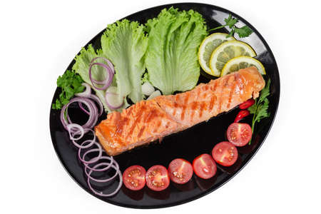 Grilled piece of the trout fillet with lemon, vegetables and greens served on the black dish on a white background, top view
