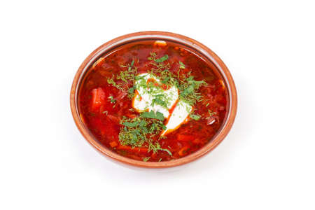 Typical red beetroot borscht seasoned with sour cream and sprinkled with fresh chopped herbs served in the ceramic bowl on a white backgroundの写真素材