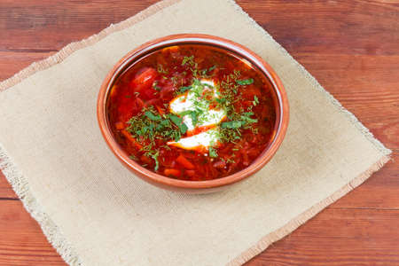 Typical red beetroot Ukrainian borscht seasoned with sour cream and sprinkled with fresh chopped herbs served in the ceramic bowl on napkin on the rustic tableの写真素材