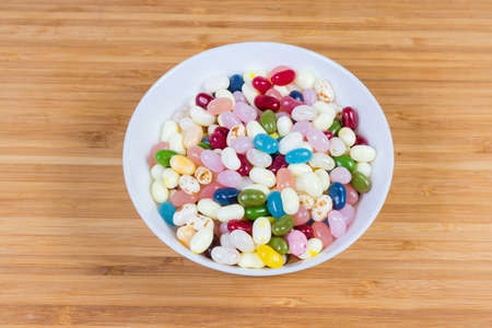 Varicolored candies jelly beans in the white bowl on the wooden surface, top view