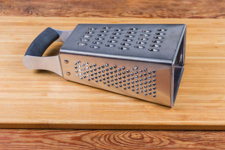 Stainless steel box-shaped four-sided kitchen grater lies on the wooden cutting board on the rustic tableの写真素材