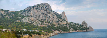 Mountain with limestone rocky outcrops covered with rare grown trees on the coast of sea against the...