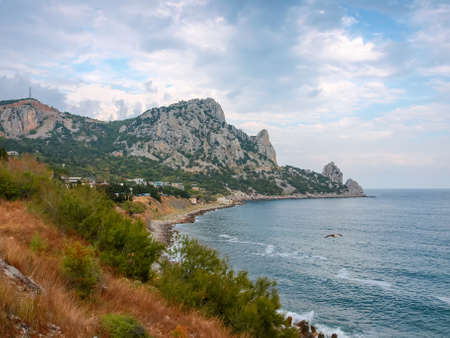 Mountain with limestone rocky outcrops covered with rare grown trees on the coast of sea against the cloudy sky in autumnの写真素材