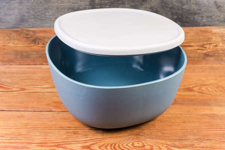 Empty plastic blue-gray salad bowl with slightly open gray lid on the rustic tableの写真素材