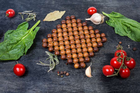 Wooden stand under the hot kitchen utensils made of juniper beads connected into the mat on a dark surface among the spices, tomatoes and spinachの写真素材