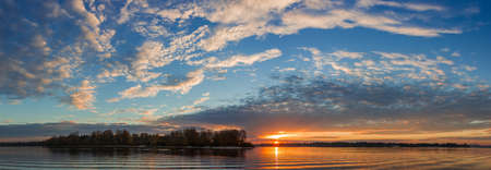 Wide river with banks overgrown with forest in autumn during sunrise, wide panoramic view