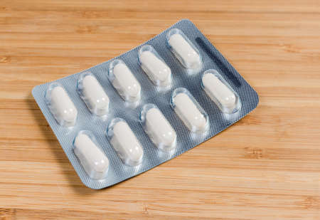 Blister pack with a pharmaceutical drug in the form of white pills on the wooden surface