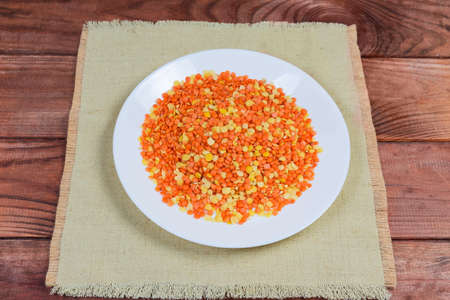 Mix of raw red and yellow split lentils on white dish on the rustic table