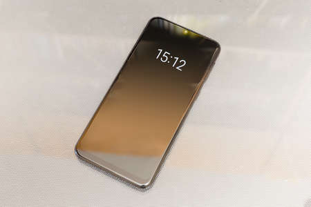 Modern smartphone with switched on dark lock screen with digital clock image on the light surface