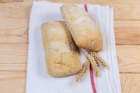 Two whole ciabatta and wheat ears on the fabric napkin on the rustic table