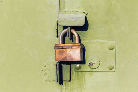 Old slightly rusty locked padlock hanging on the closed metal gate outdoors