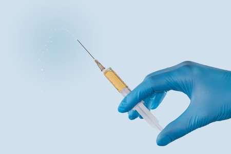Plastic disposable medical syringe with hypodermic needle filled with drug in a hand wearing a blue nitrile medical glove before injection on a light backgroundの写真素材